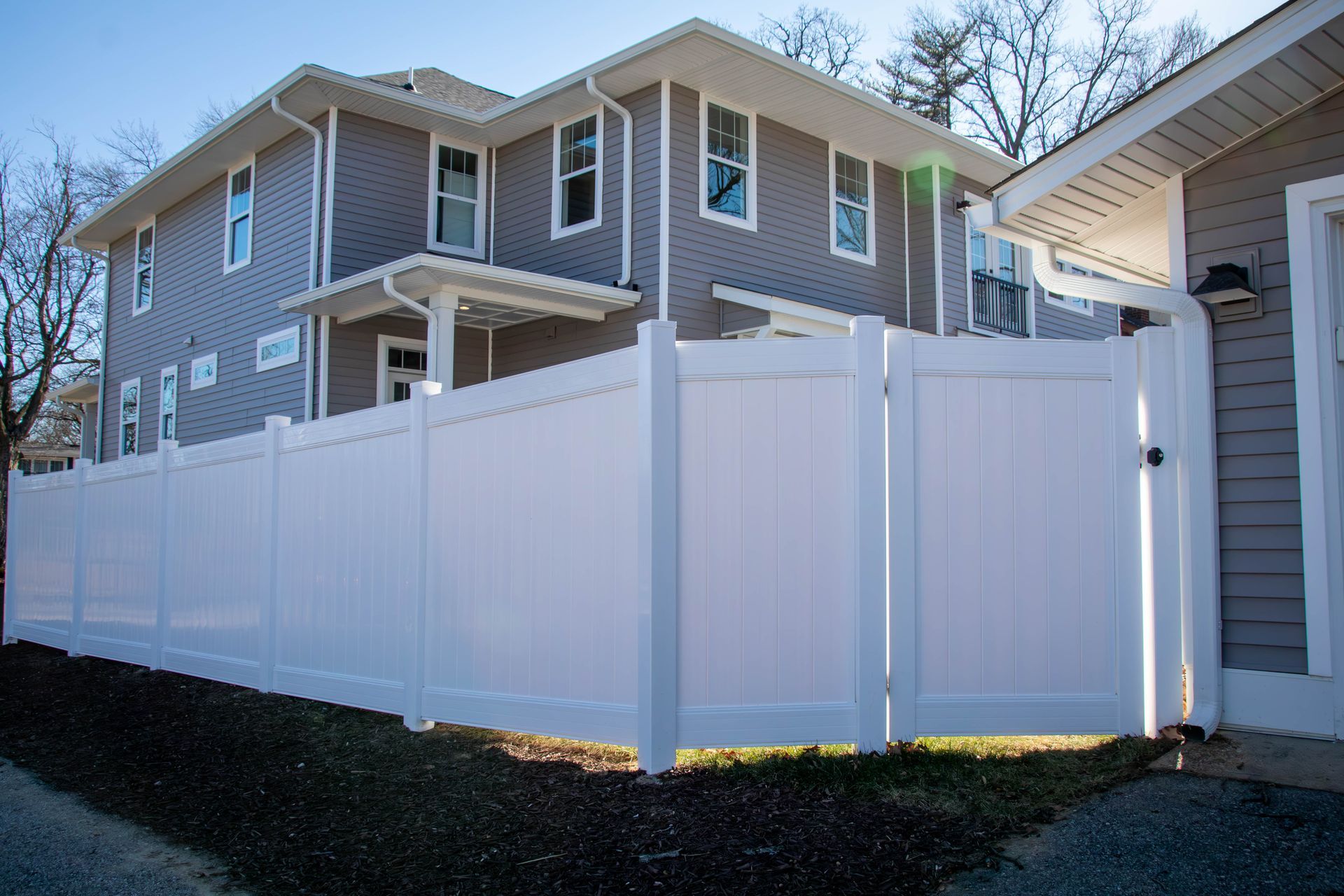 White vinyl fence surrounds a gray two-story house with a white trim.
