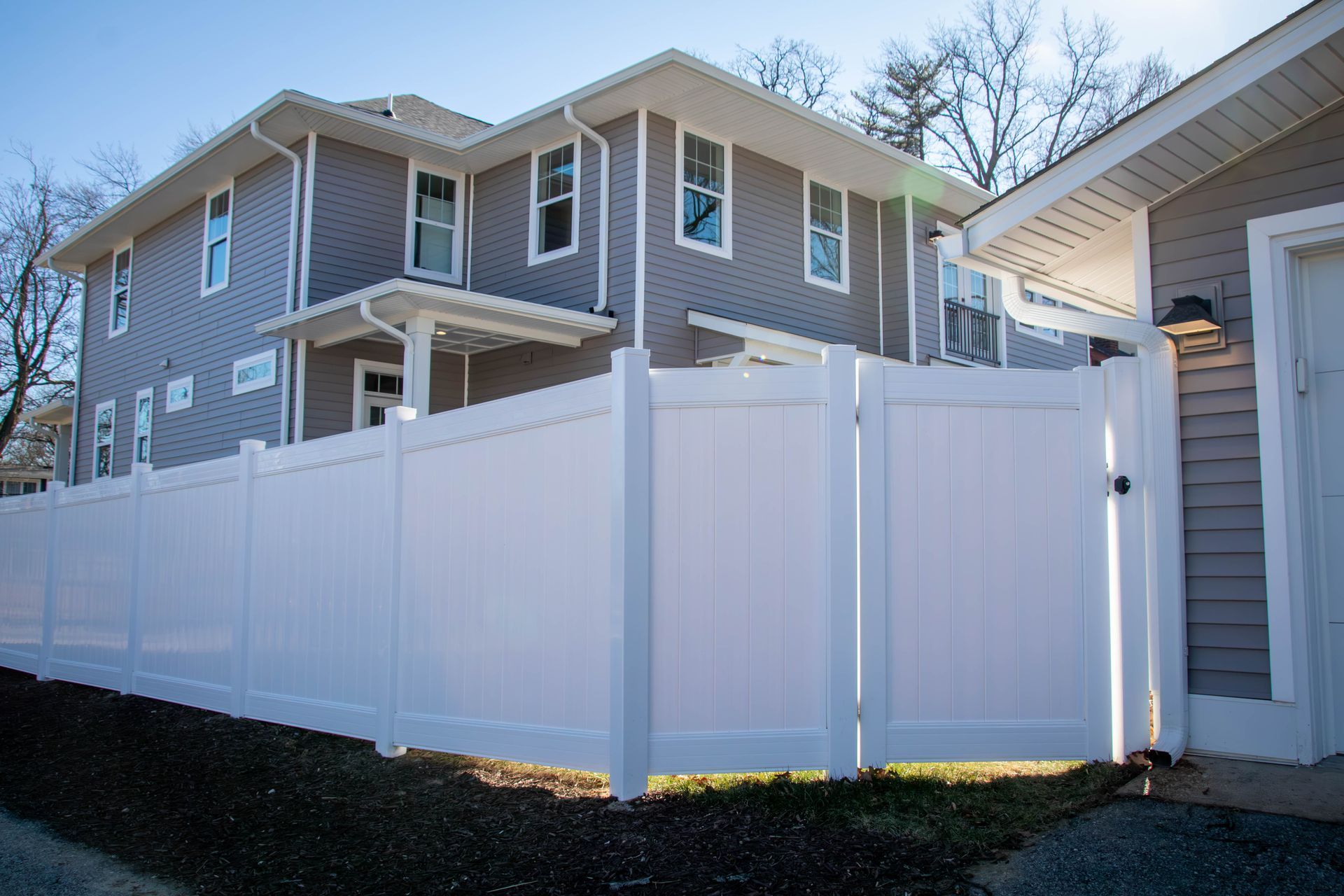 White fence around a two-story gray house with a small garage.
