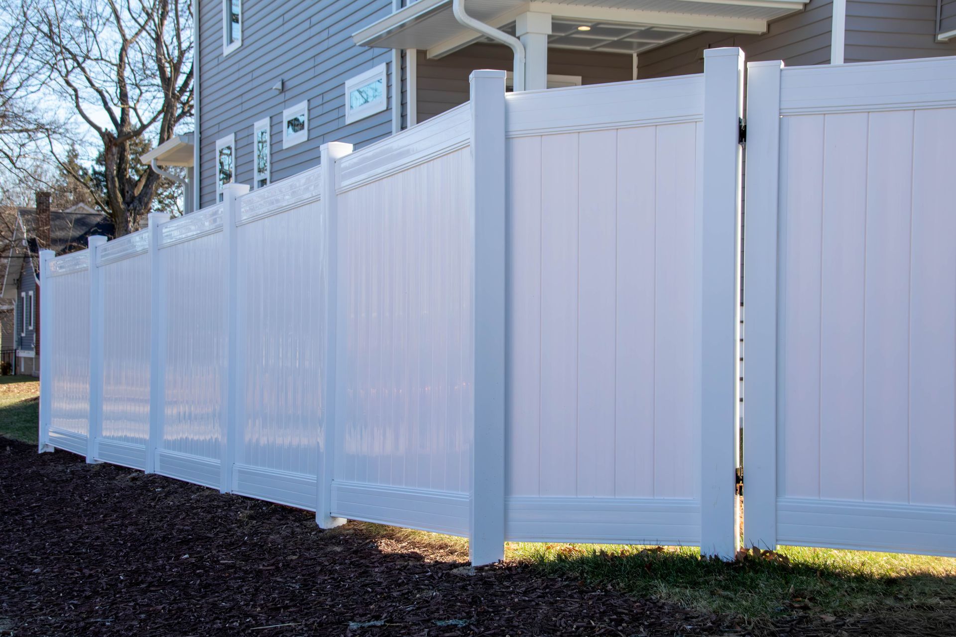 White vinyl fence with a gate, bordering a grassy area and building.