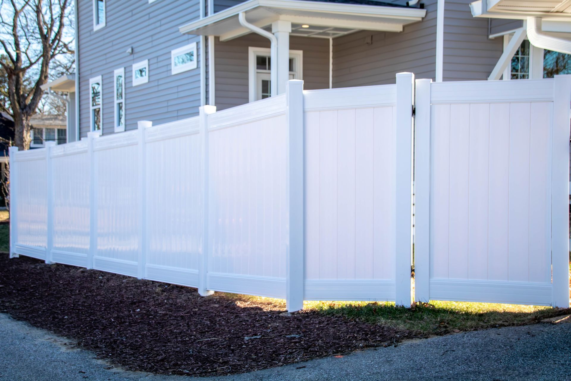 White vinyl privacy fence in front of a gray house.