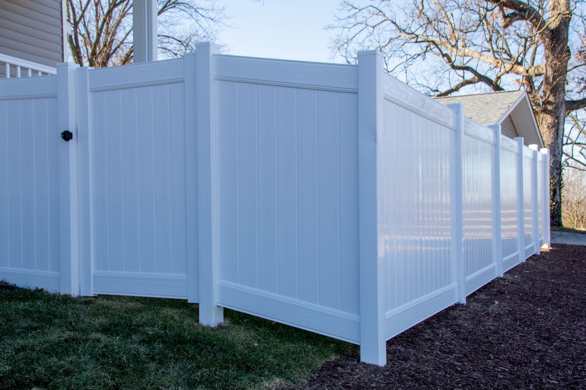 White vinyl fence around a yard, framing a house and trees.