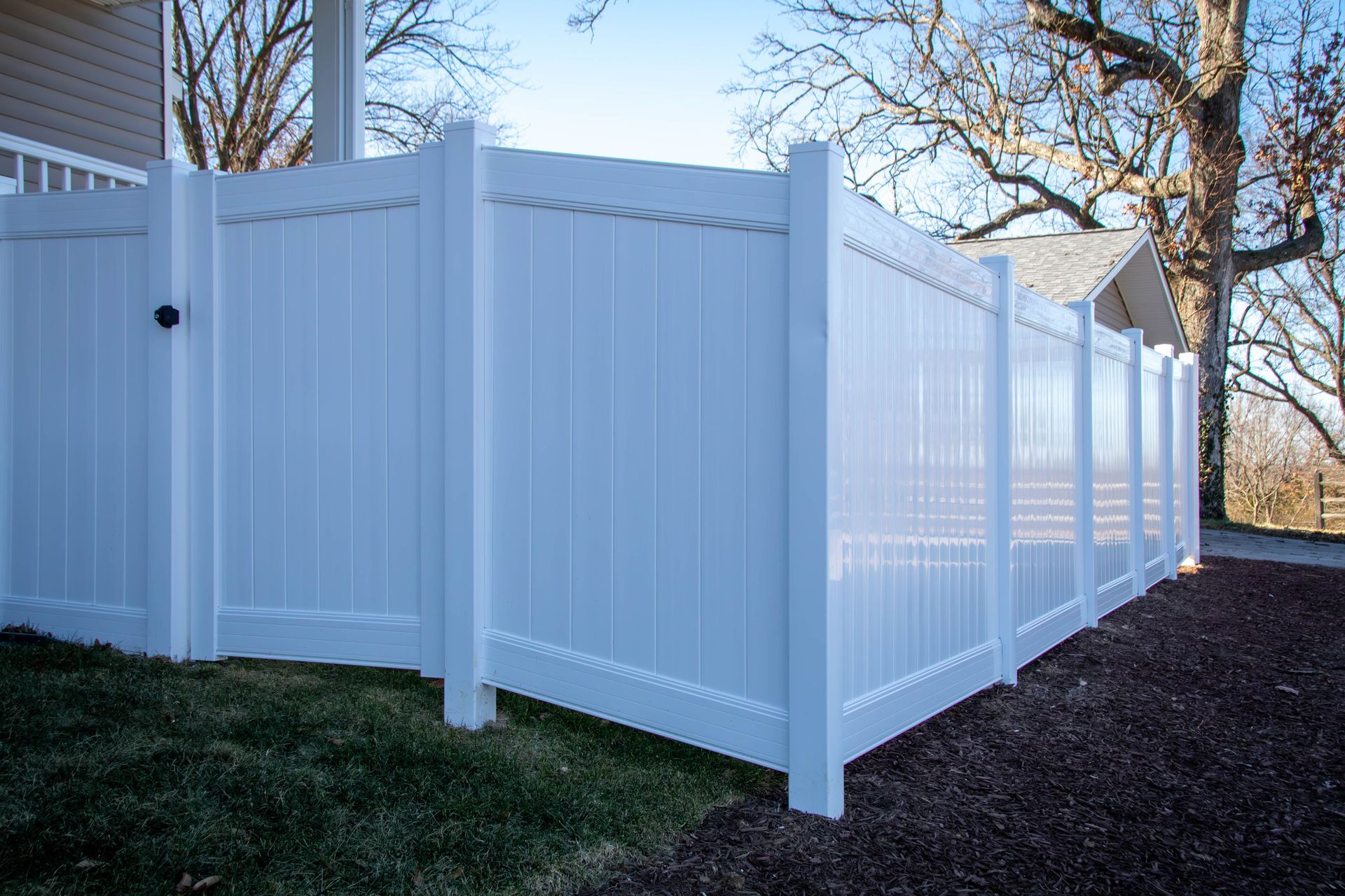 White vinyl privacy fence around a grassy yard and small trees.