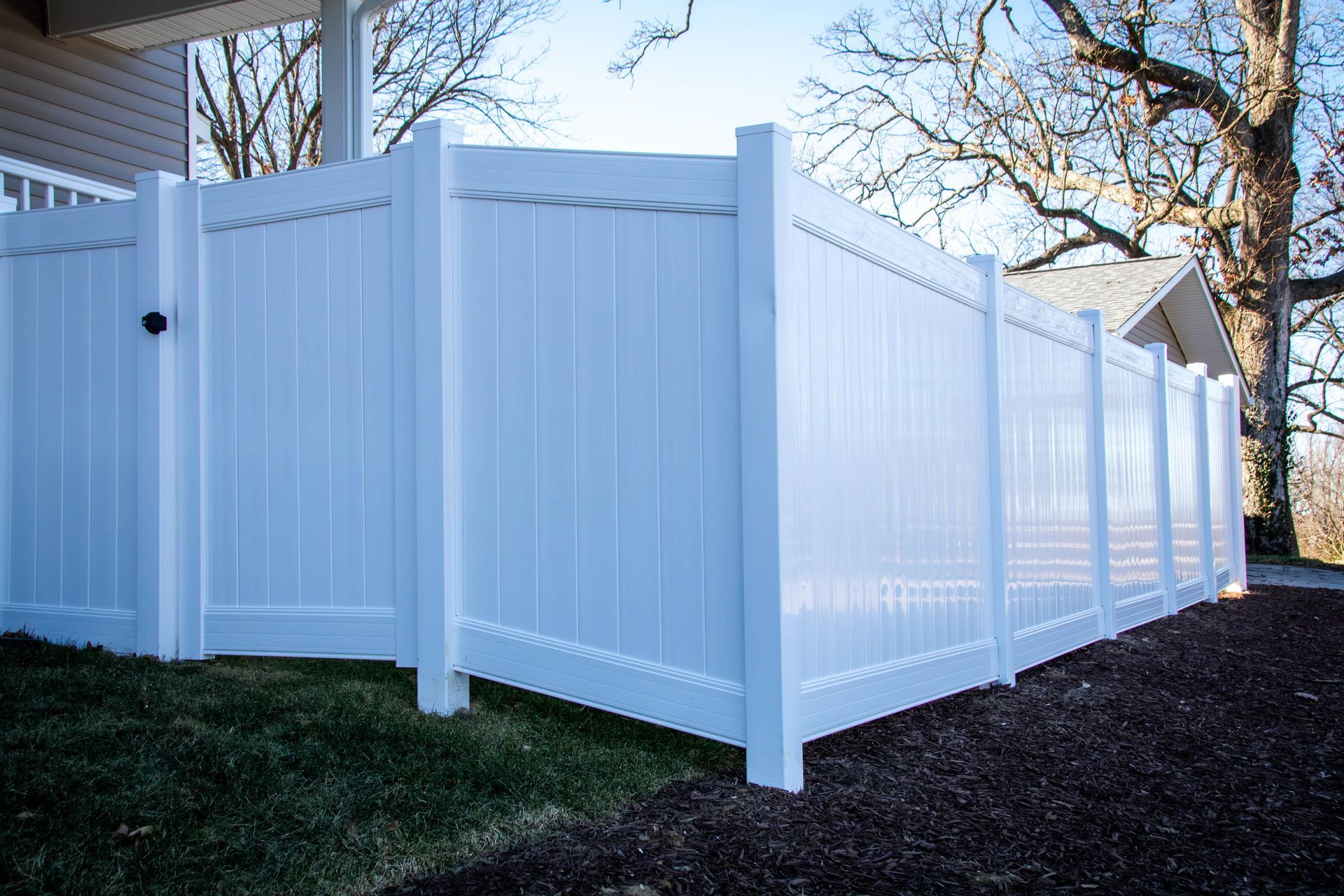 White vinyl privacy fence around a grassy yard and mulch.
