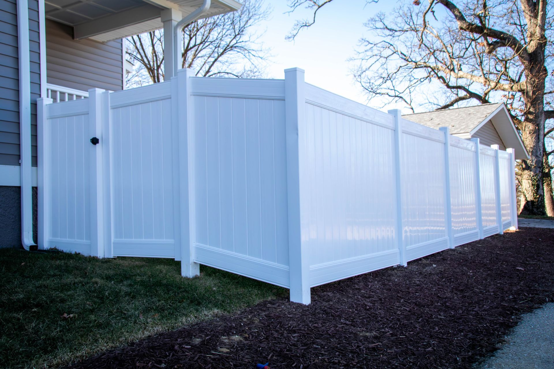 White vinyl privacy fence surrounding a house on a grassy lawn.