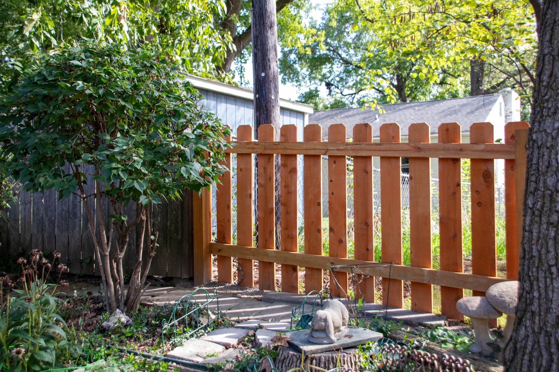 Wooden picket fence in a garden setting, partly blocking the view of a shed.