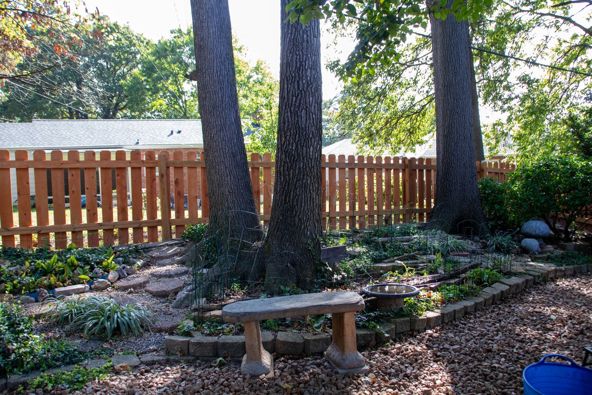 Stone bench in a backyard garden with trees, a fence, and landscaping.