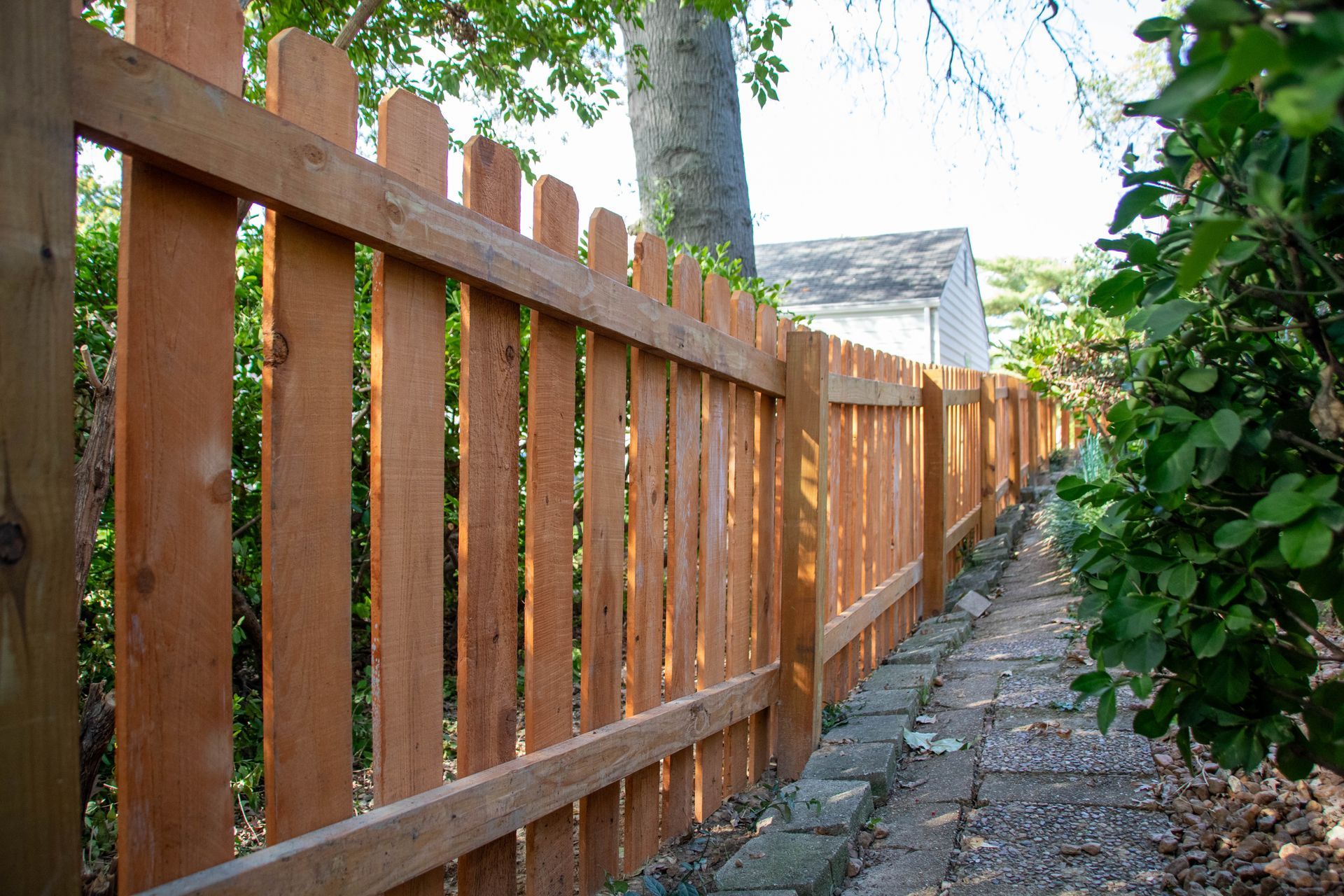 Wooden picket fence along a brick pathway.
