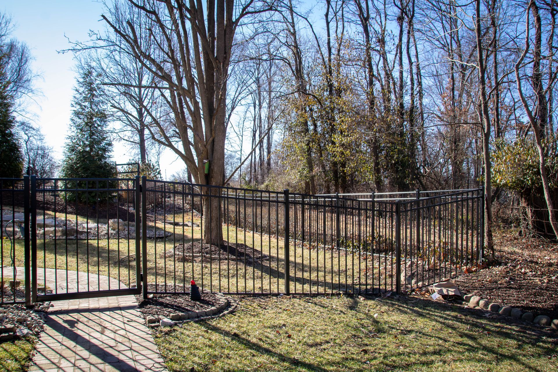 Black metal fence encloses backyard, trees in background, sunny day.