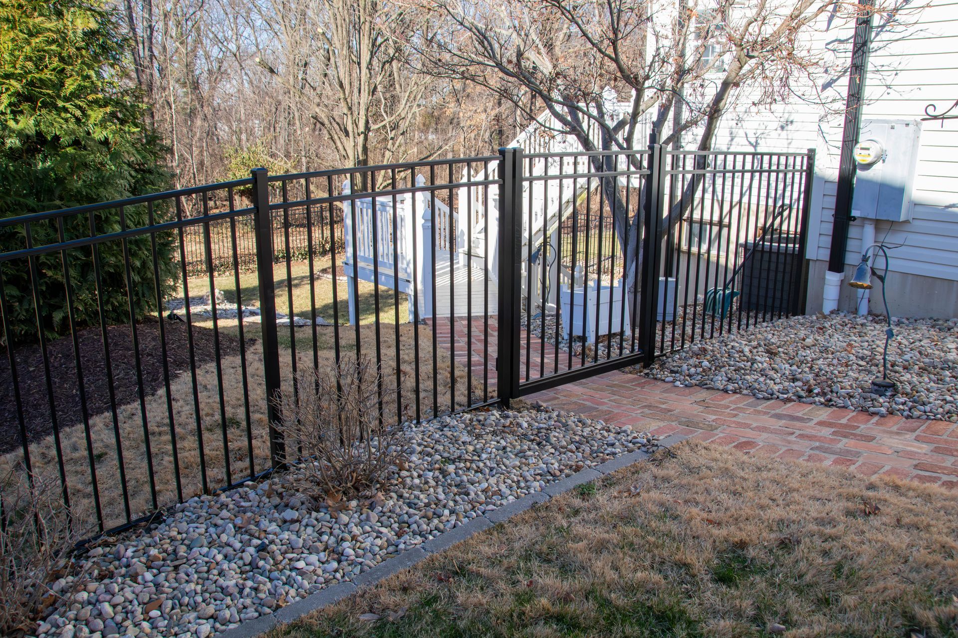 Black metal fence surrounding a yard with a gate, rocks, and dried grass.