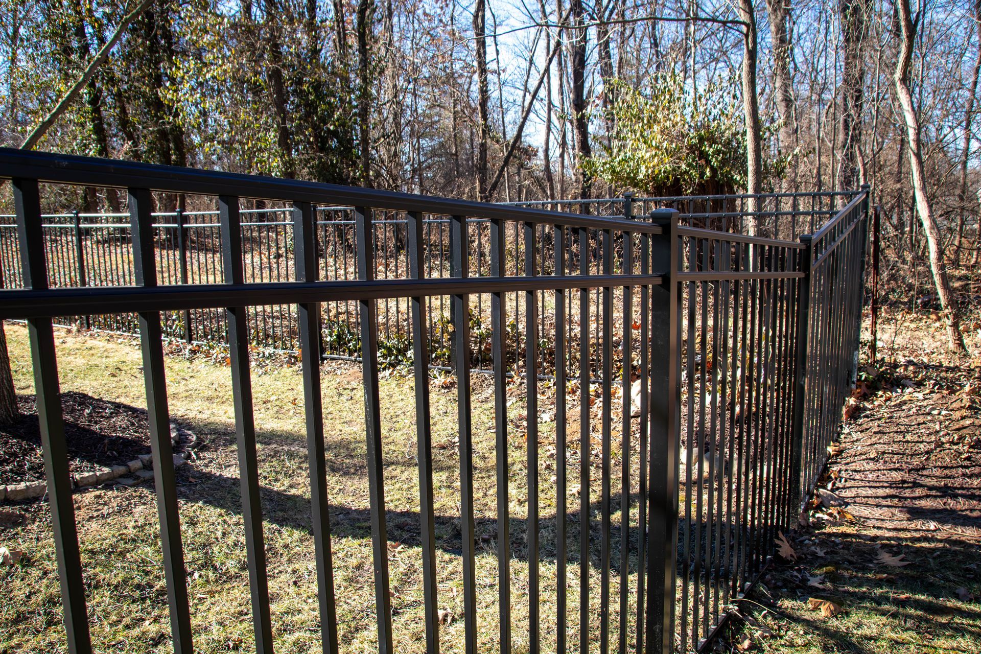 Black metal fence in a yard, with trees and grass in the background. Sunny day.