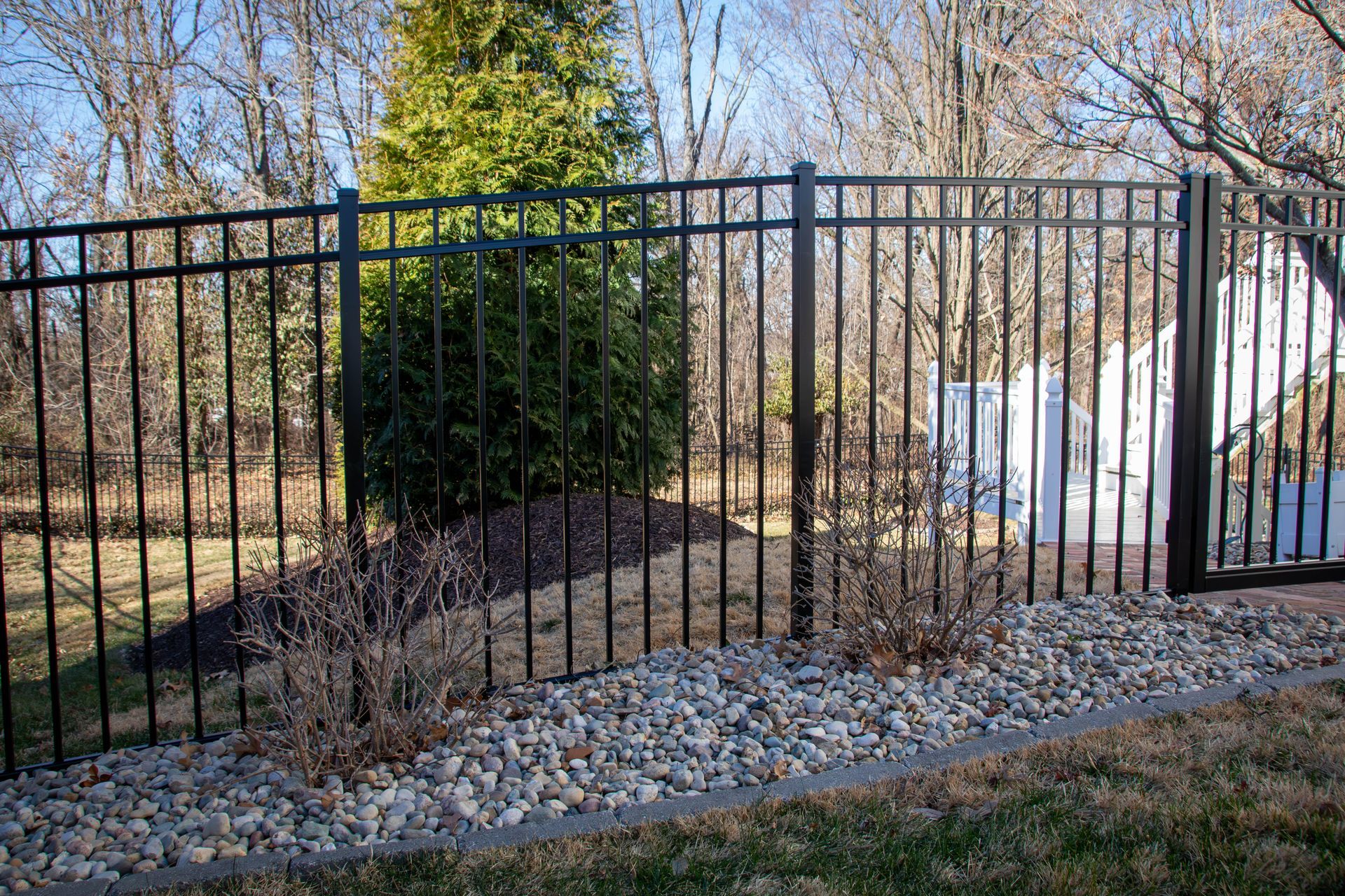 Black metal fence bordering a yard with rocks and dried plants in front of a tree.