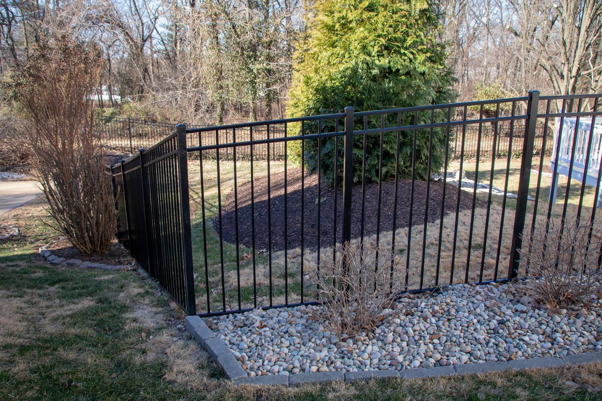 Black metal fence around a landscaped area with a green bush and gravel.