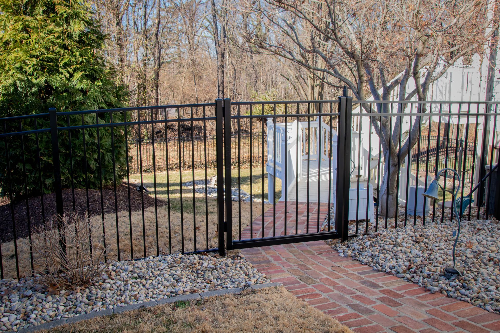 Black metal gate and fence enclose a backyard with a brick walkway and trees.