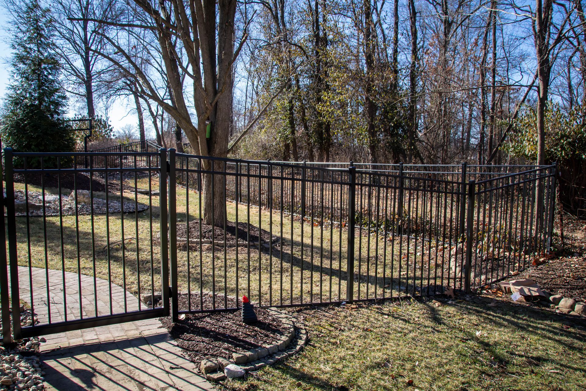 Black metal fence enclosing a grassy yard, with trees in the background under a bright sky.