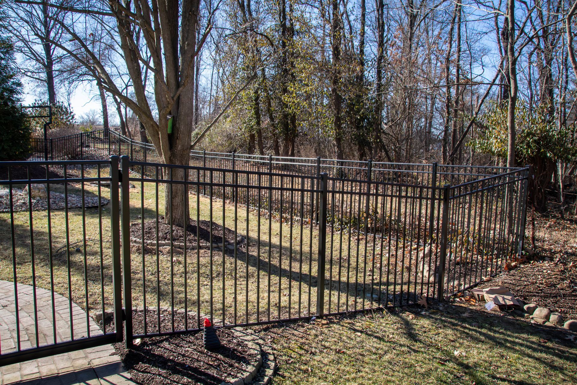 Black metal fence in a yard, trees in the background, sunny day.