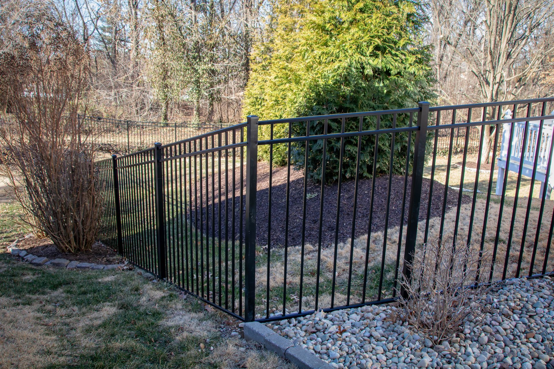 Black metal fence bordering a yard with shrubs, trees, and ground cover.