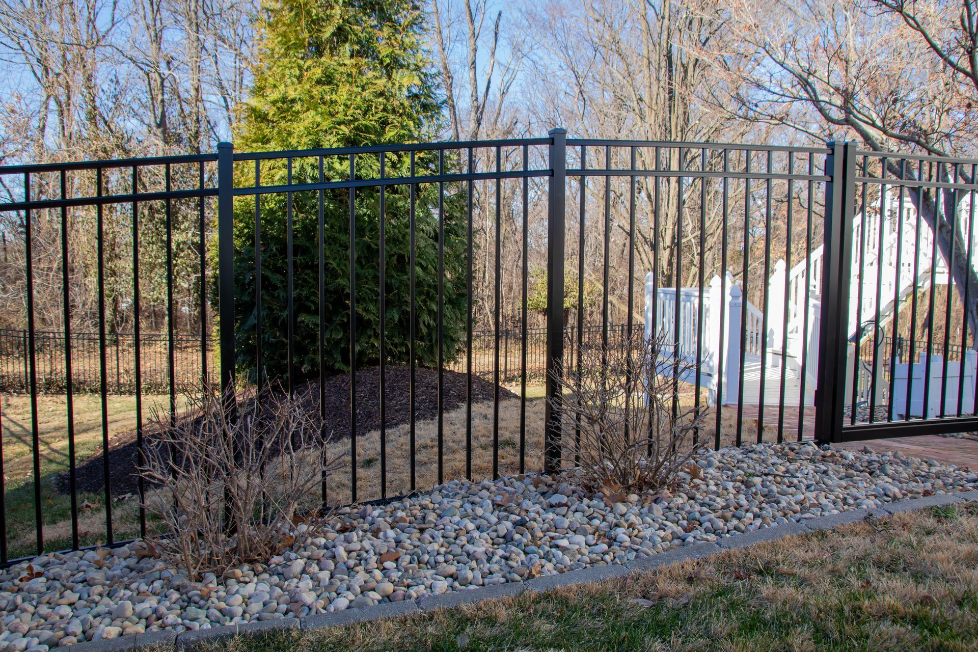 Black metal fence surrounds a yard with a small tree and stone border.