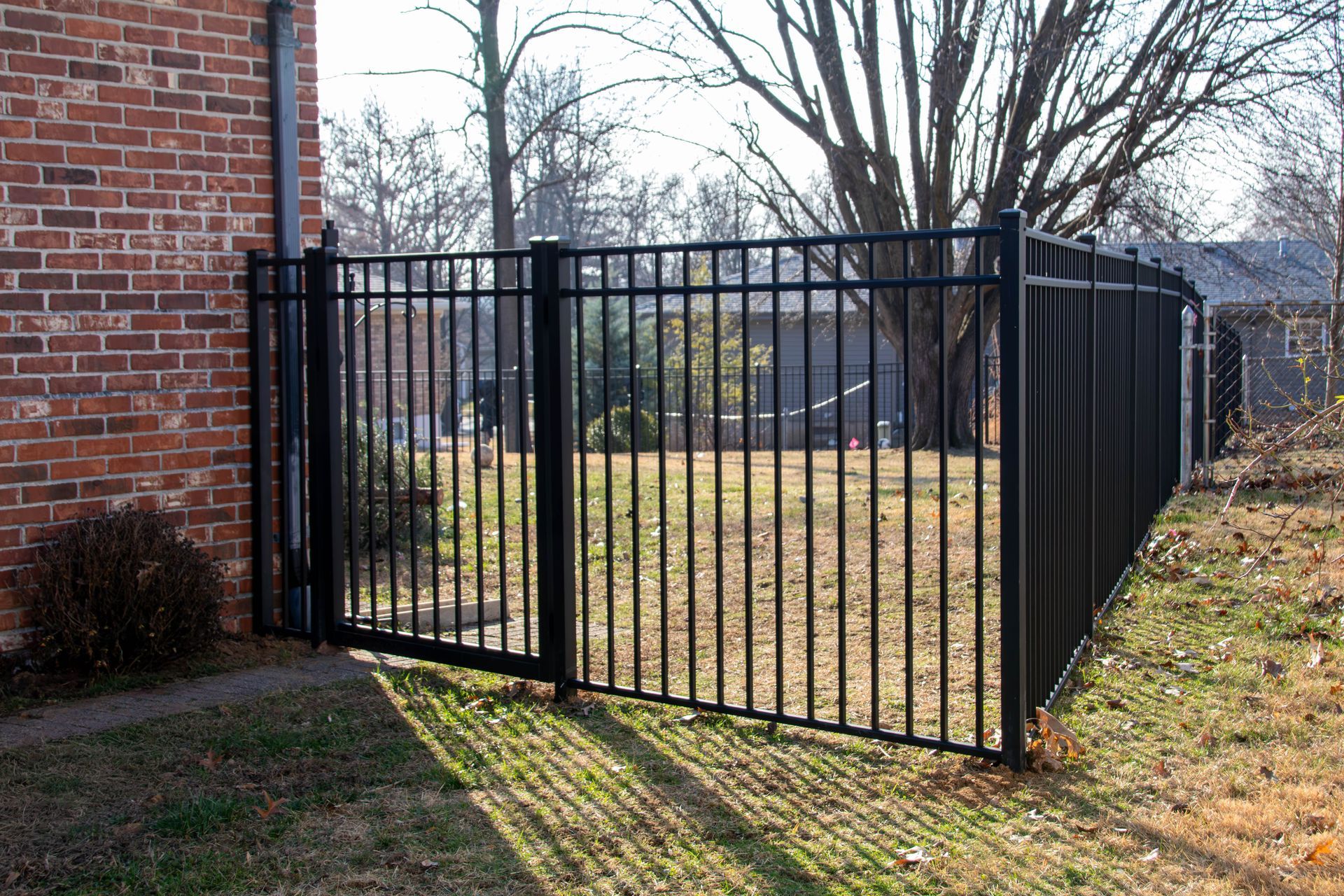 Black metal fence next to a brick building. The fence encloses a grassy area.