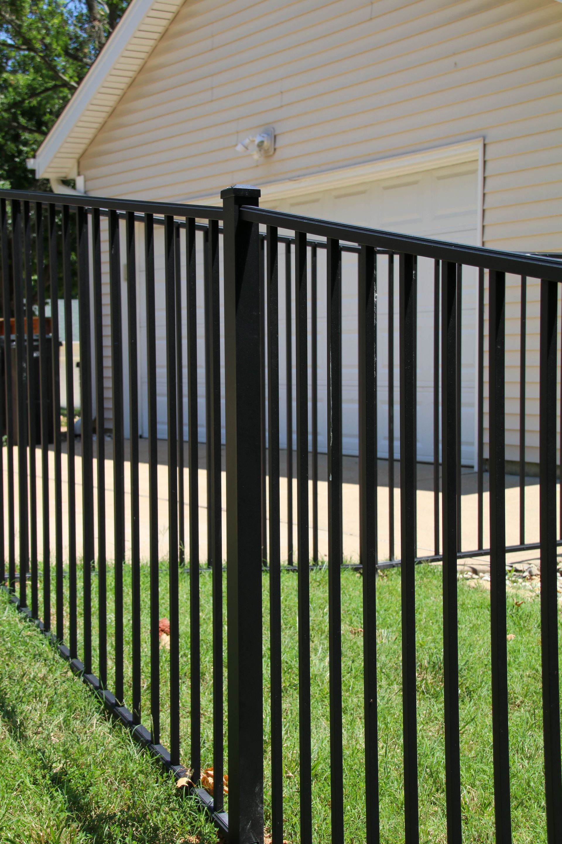 Black metal fence in front of a tan garage on a sunny day.