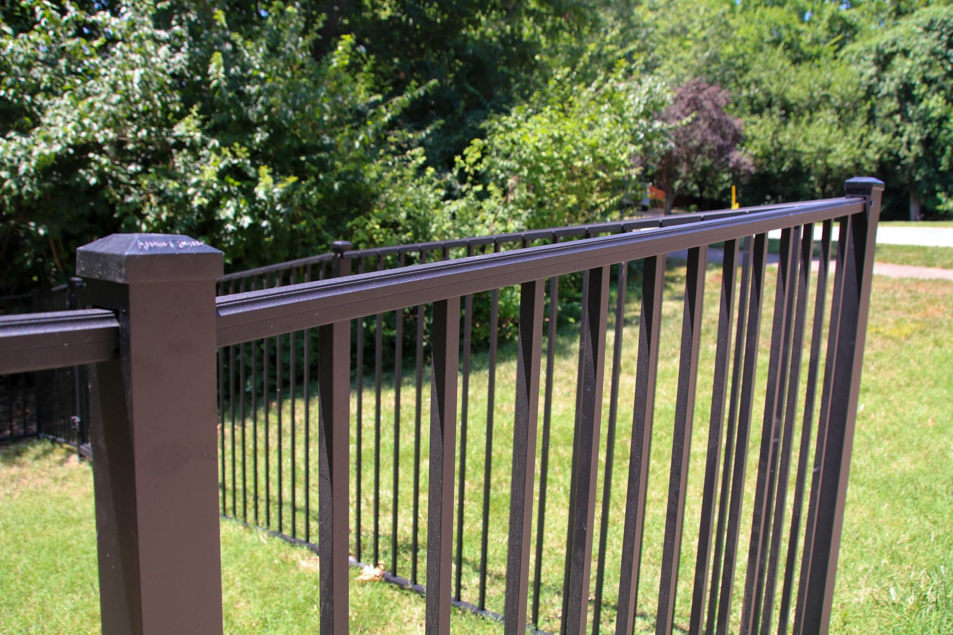 Brown metal fence with vertical bars, separating green lawn from trees.