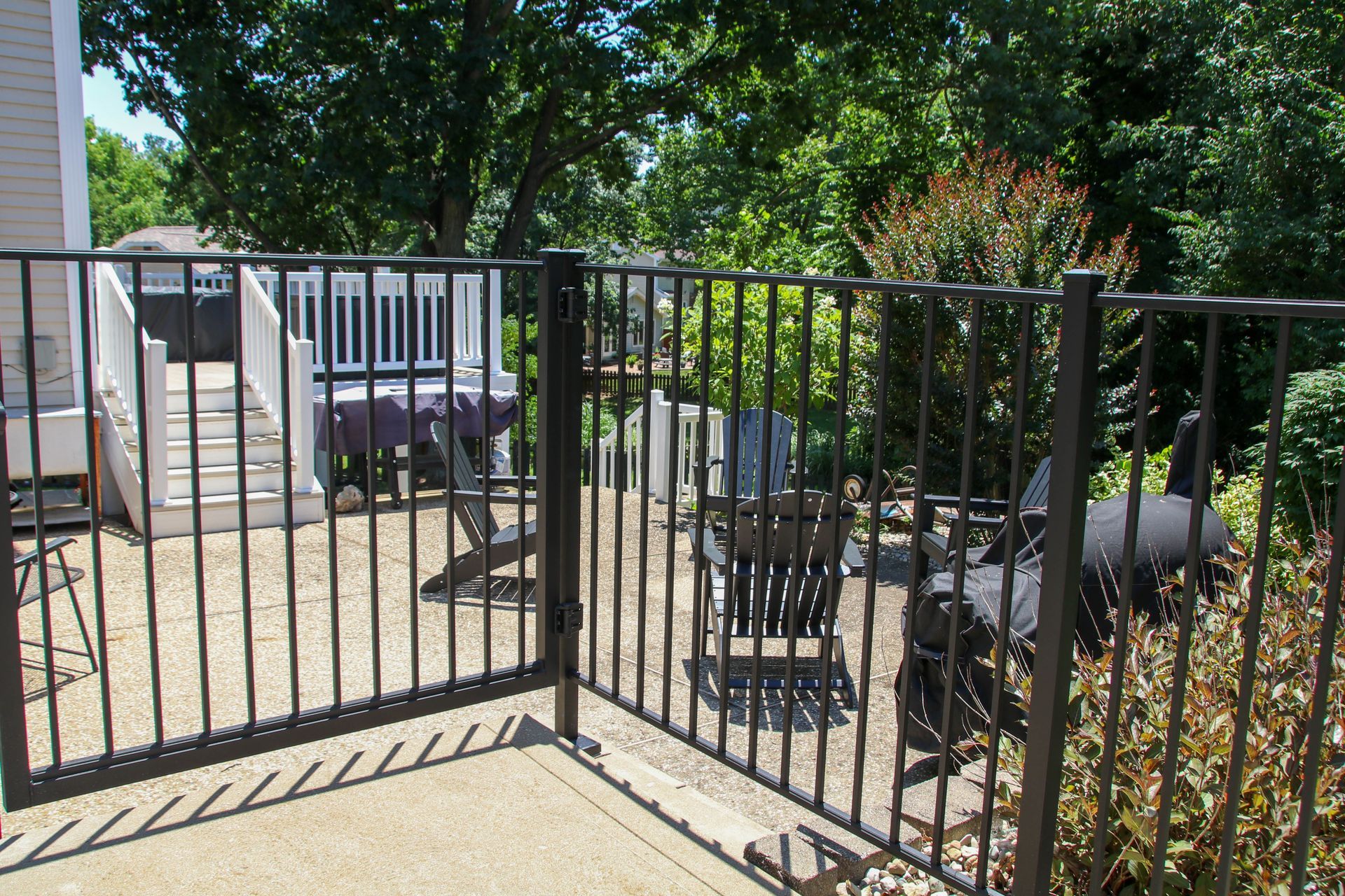Black metal fence encloses a patio with deck and grill, trees in background.