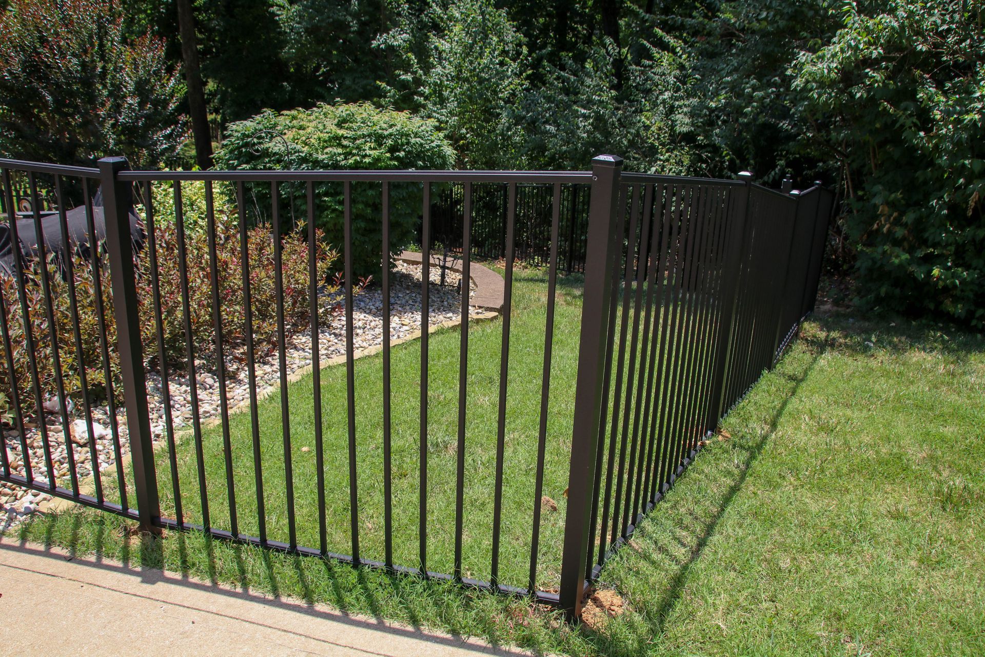 Black metal fence surrounding a yard with green grass and bushes.