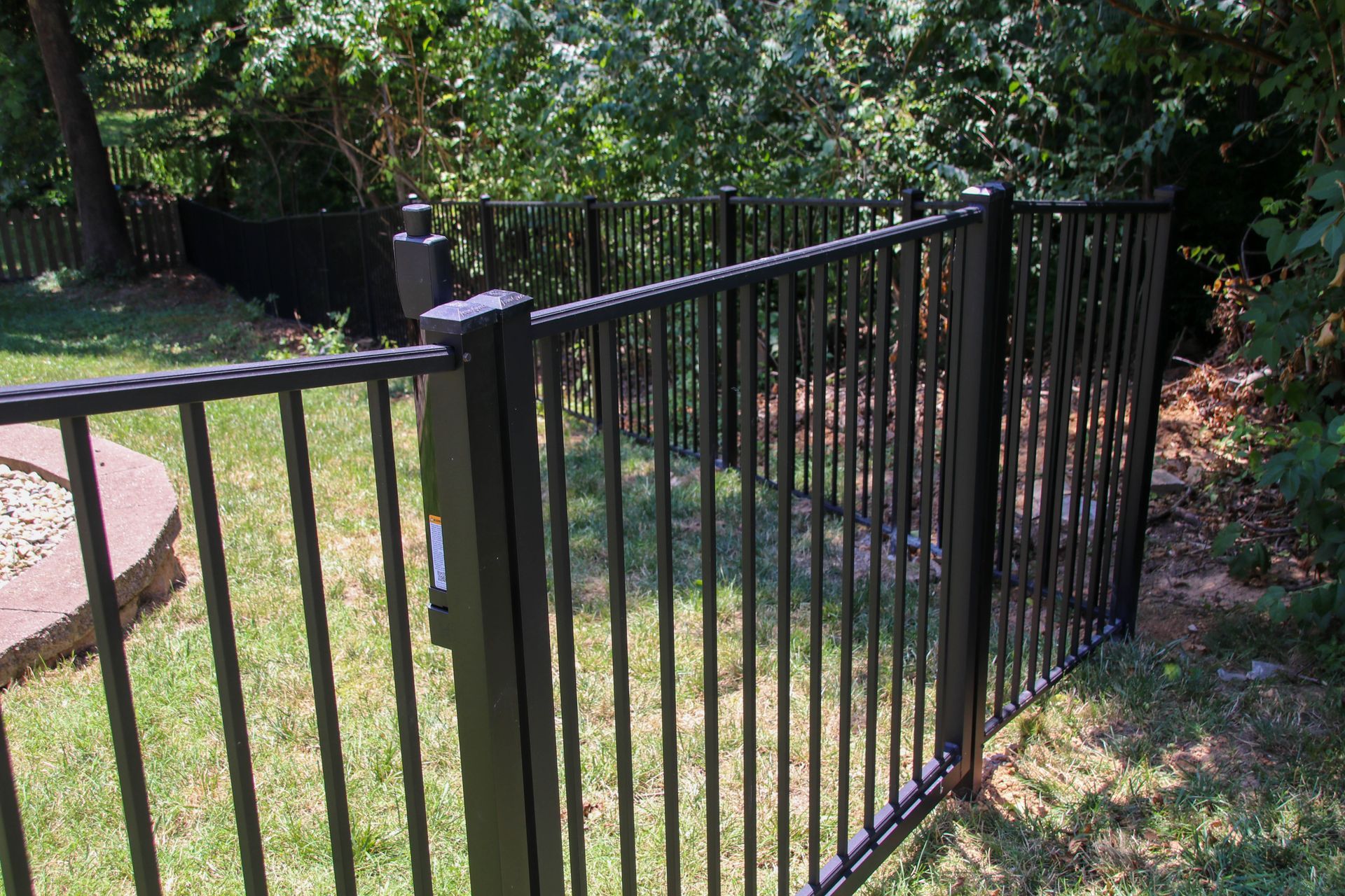 Black metal fence in a yard with grass and trees in the background.