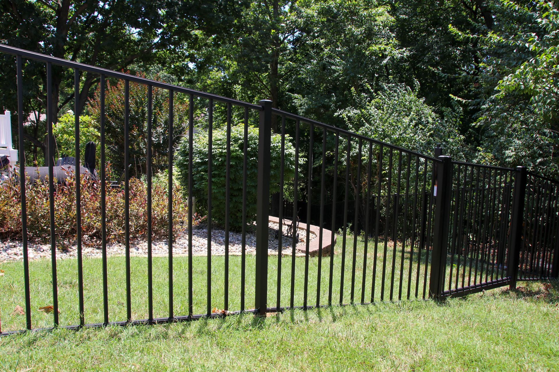Black metal fence in a yard with green grass and trees in the background.