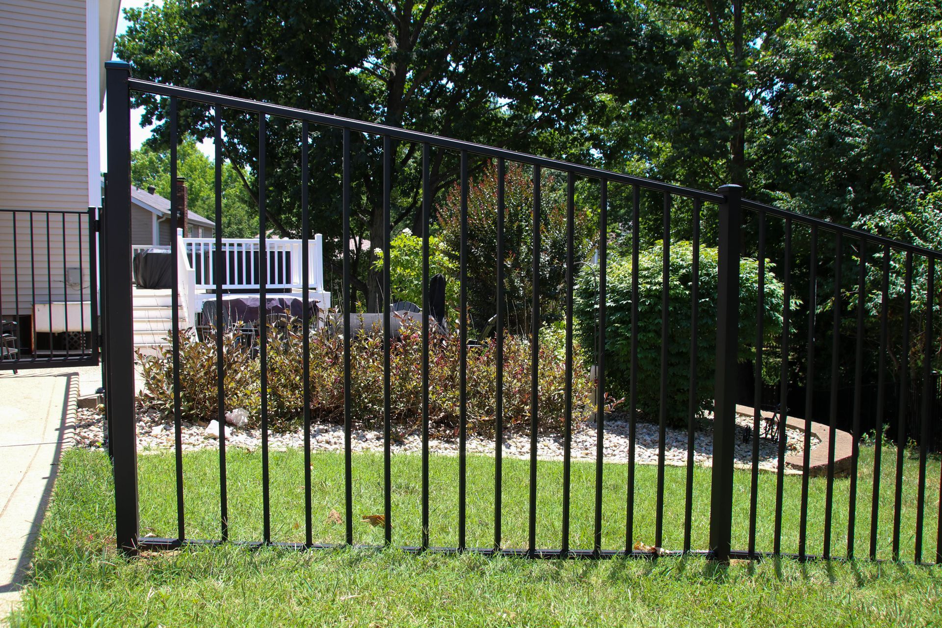 Black metal fence on green lawn, enclosing a garden with a house in the background.