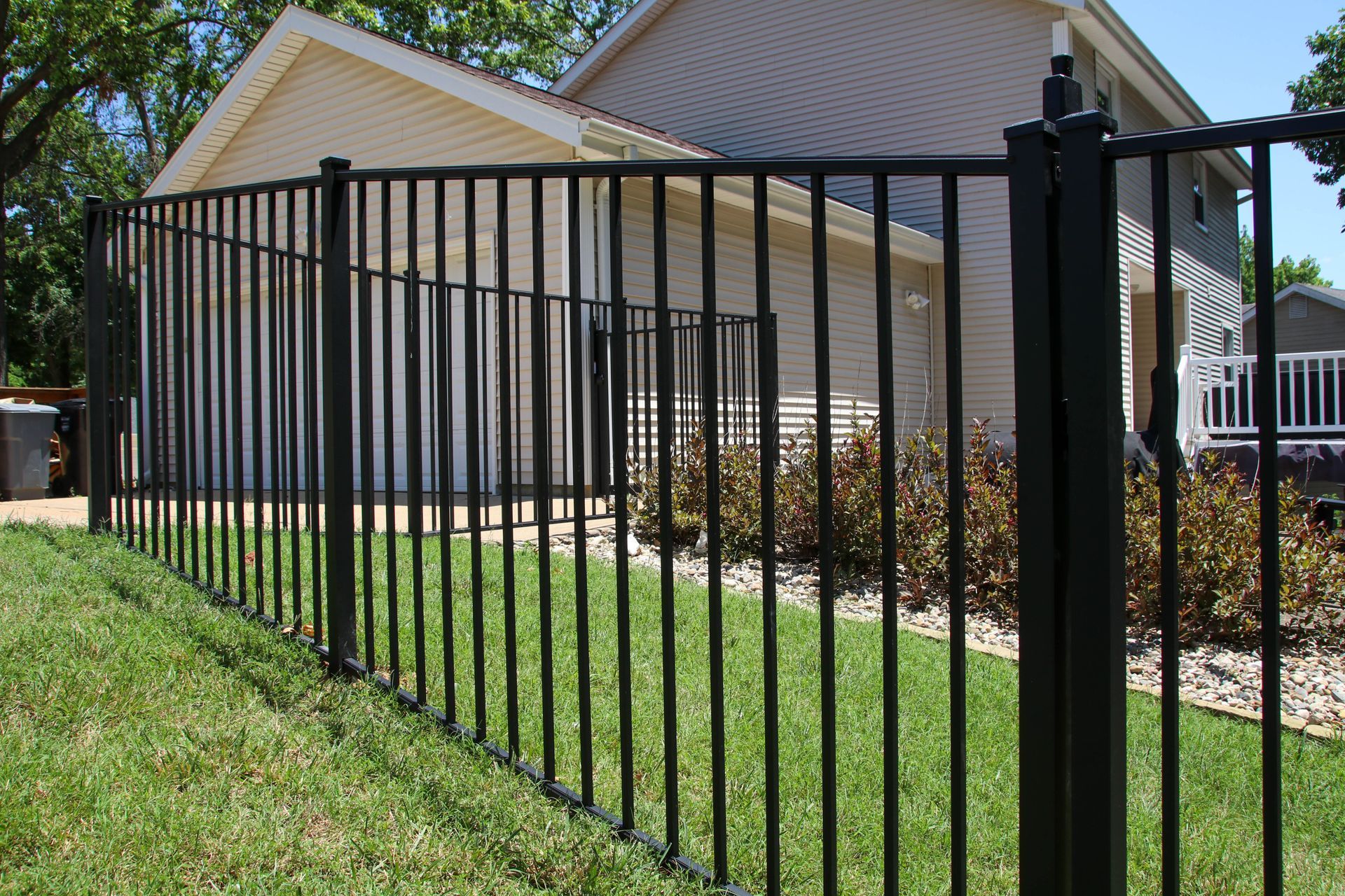 Black metal fence surrounding a house with a green lawn.