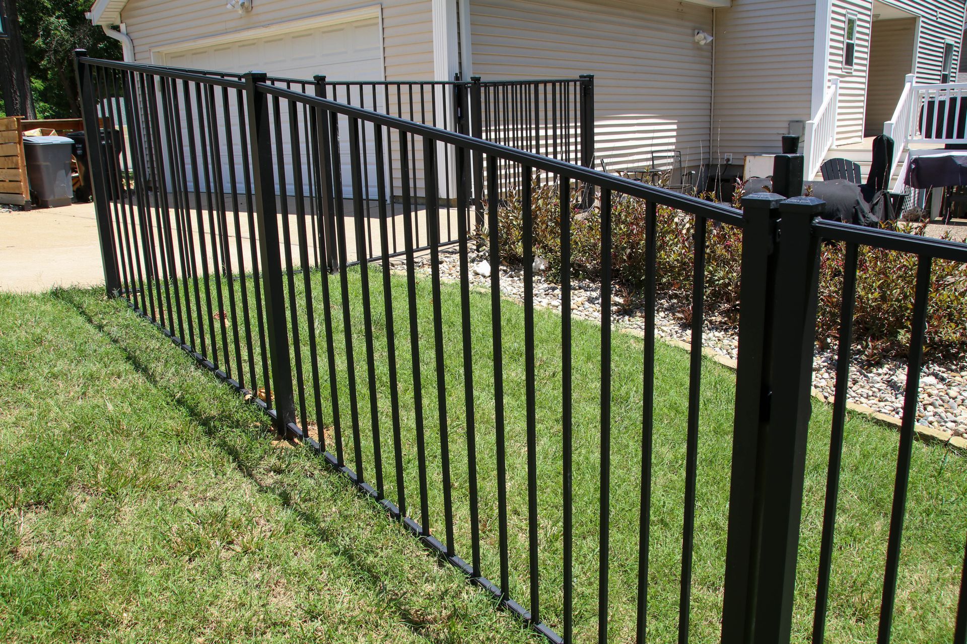 Black metal fence bordering a green lawn near a house with a garage and patio.