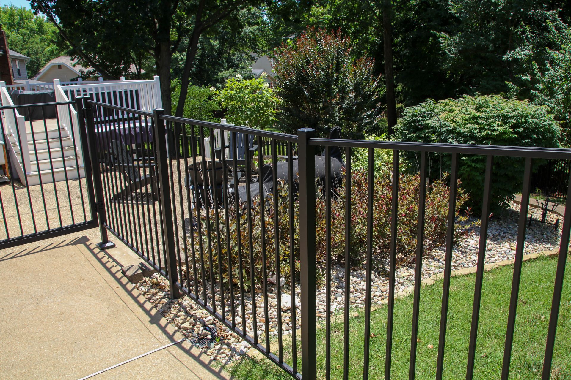 Black metal fence surrounding a garden bed on a patio. Green lawn and trees in the background.