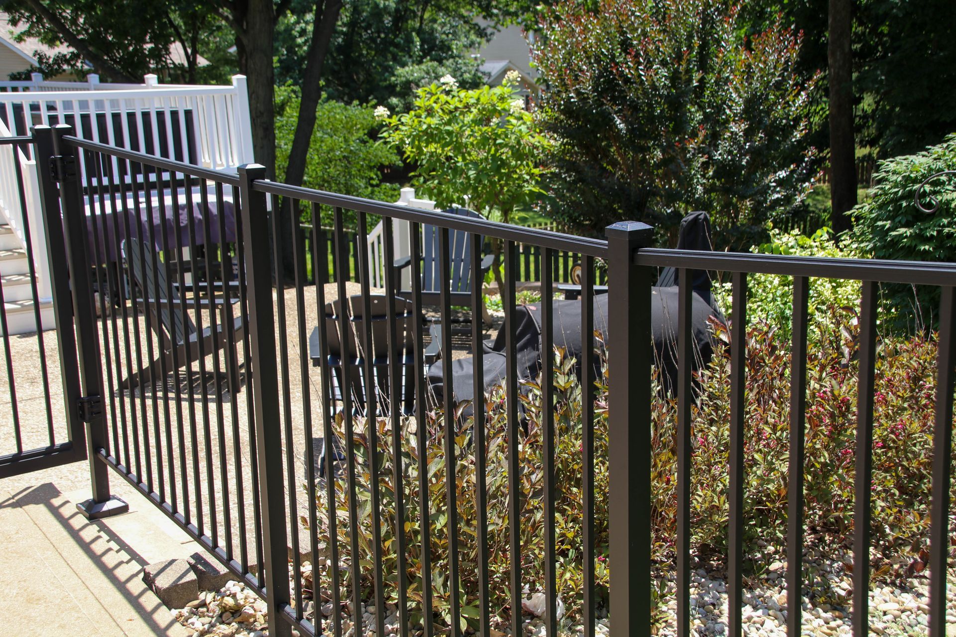 Black metal fence in a yard, with visible patio furniture and greenery in the background.