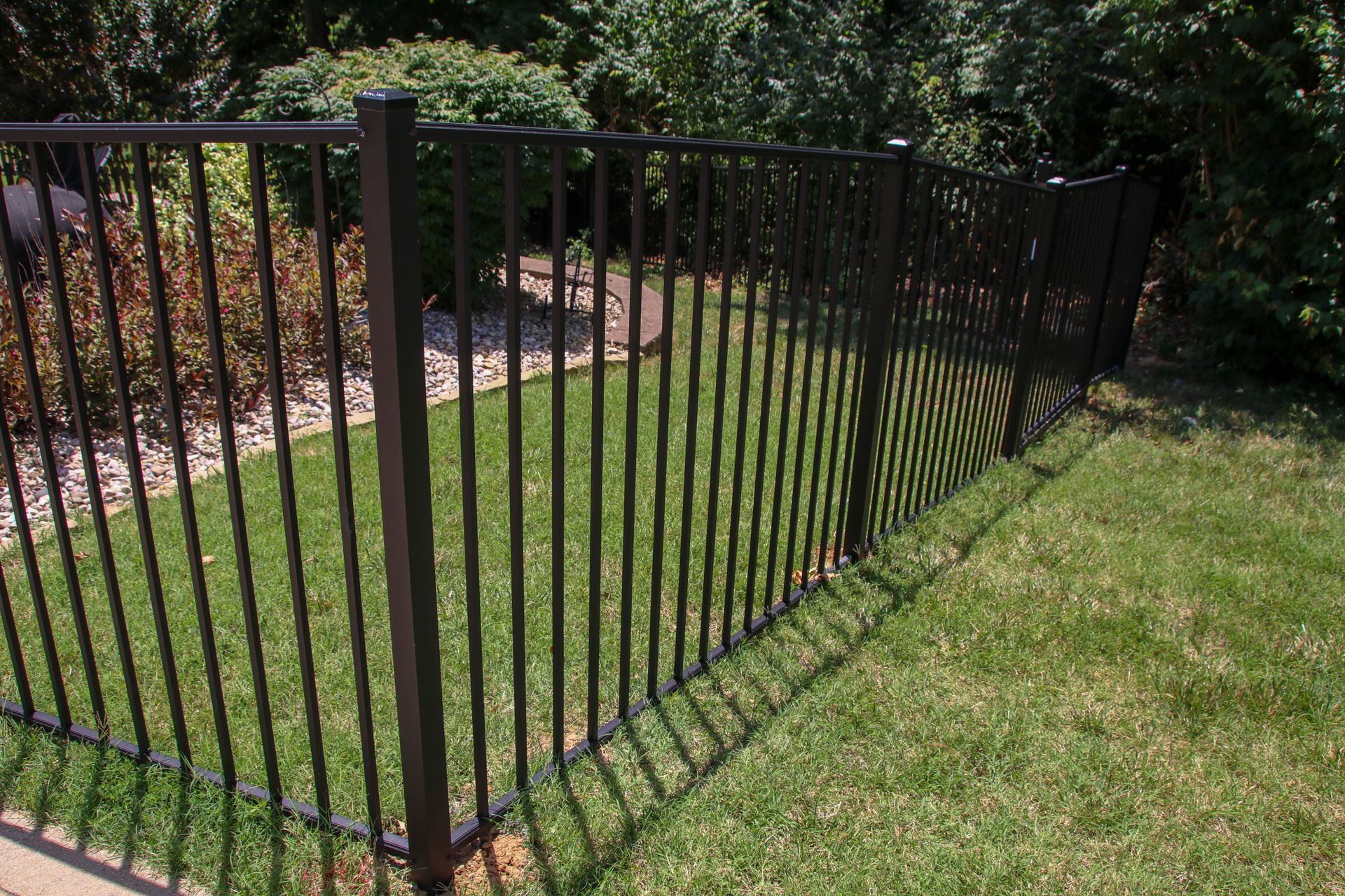 Black metal fence along green lawn, with vegetation in background.