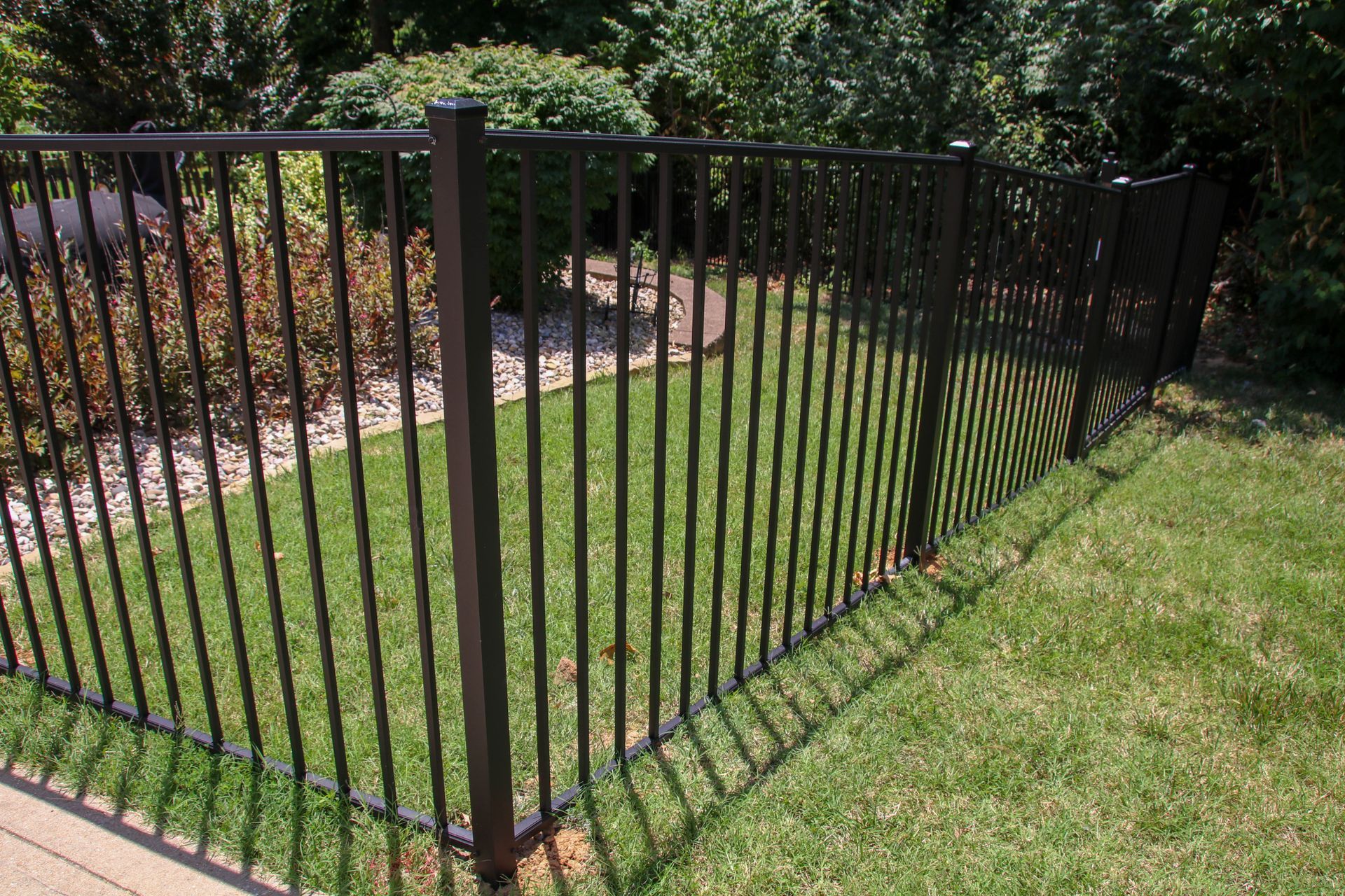 Black metal fence enclosing a grassy yard with landscaping in the background.