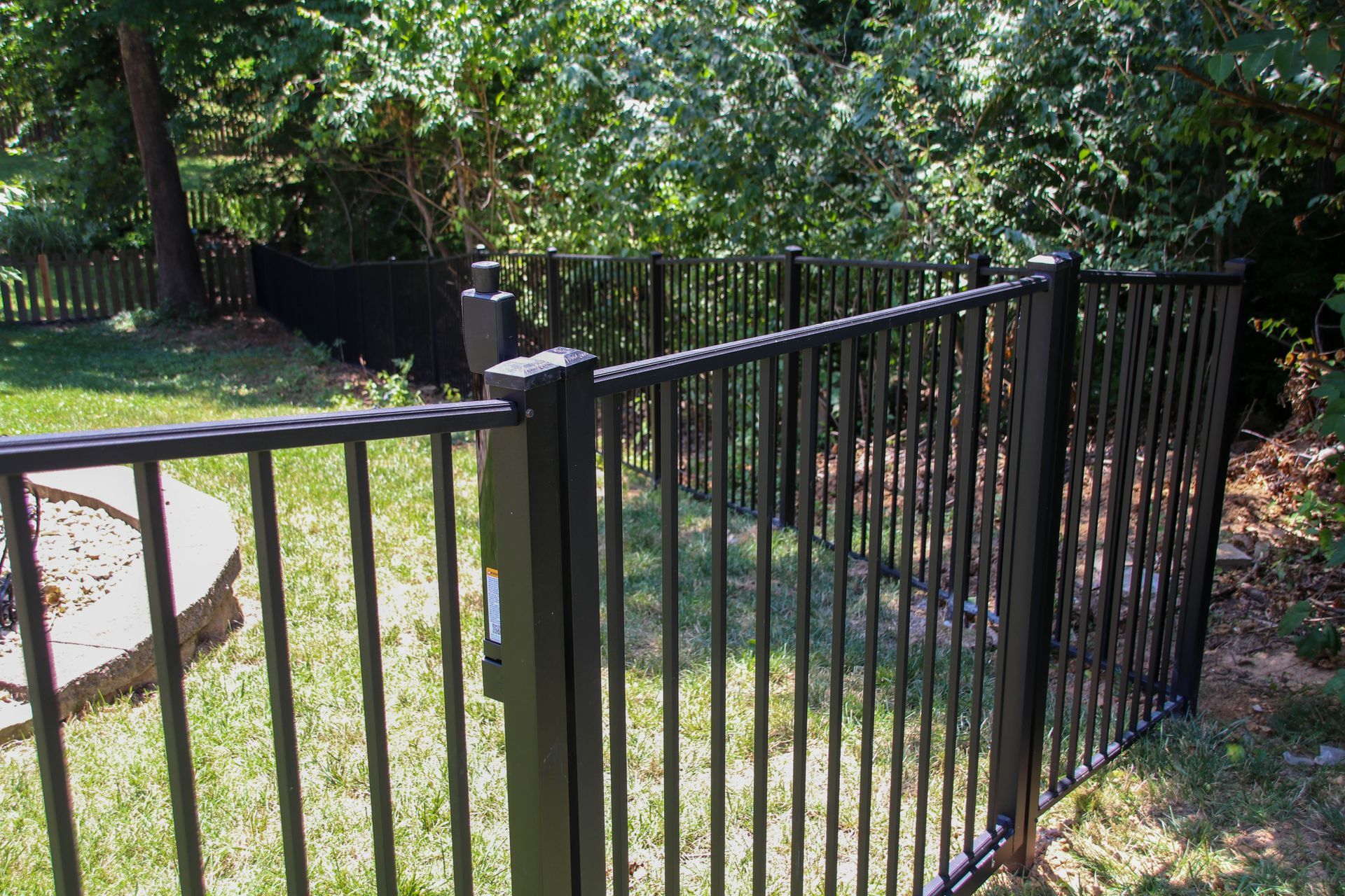 Black metal fence encloses a grassy yard with trees in the background.