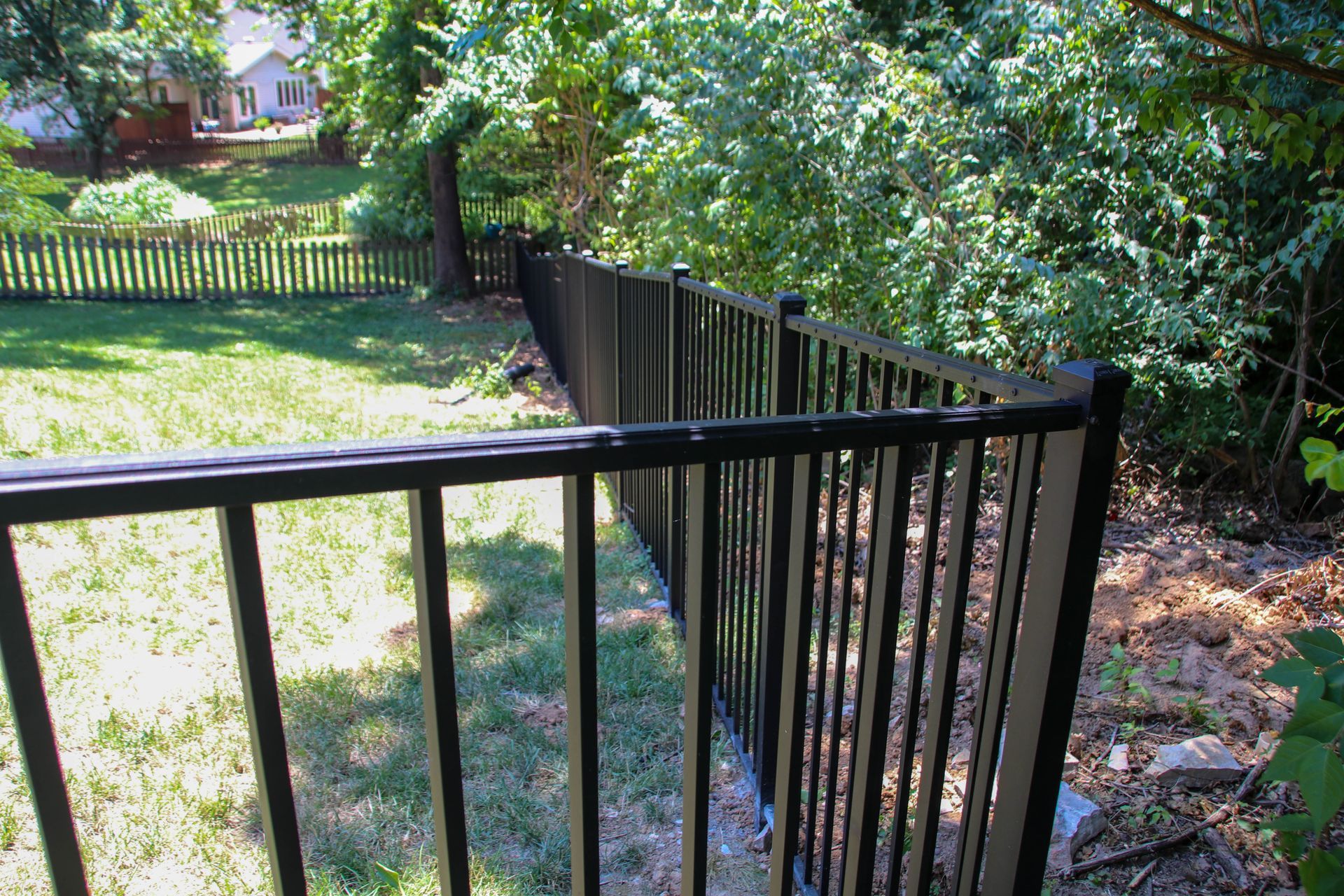 Black metal fence bordering a green grassy yard and a wooded area.