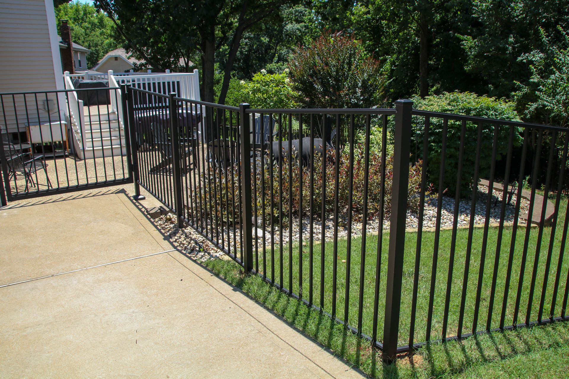 Black metal fence enclosing a backyard with a concrete patio and green grass.