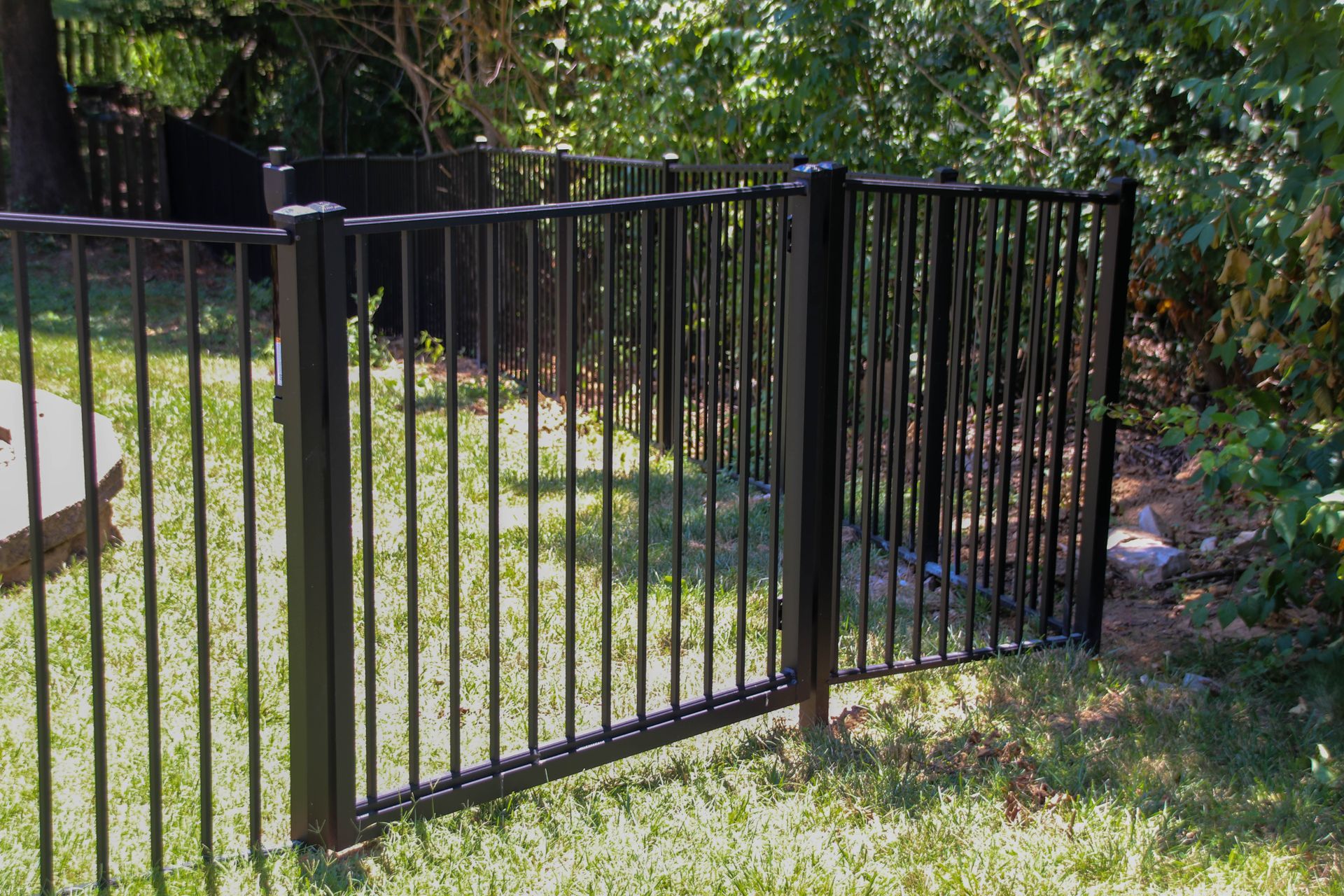 Black metal fence with a gate, in a grassy yard, near trees.