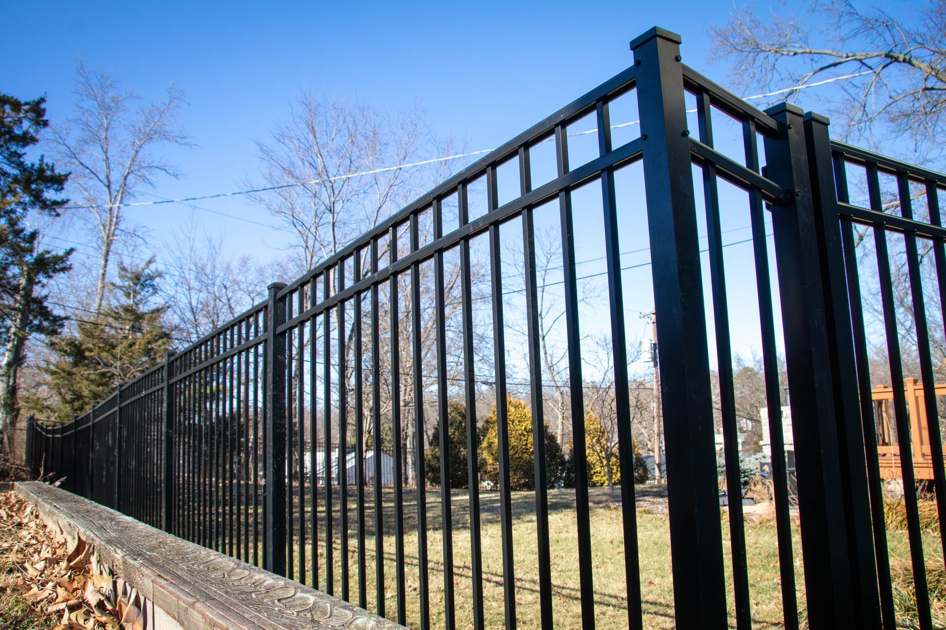 Black metal fence on a grassy lawn, with trees and a blue sky in the background.