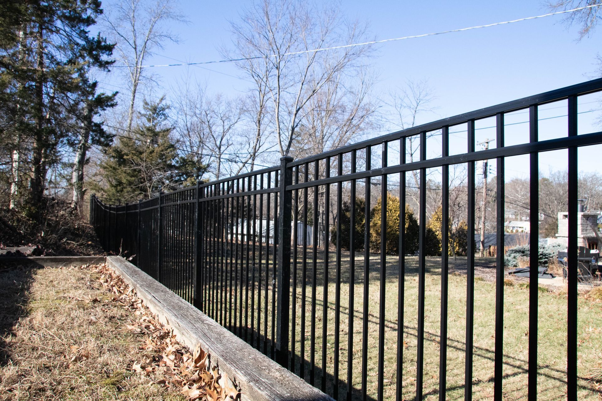 Black metal fence in a yard, with bare trees and a blue sky in the background.
