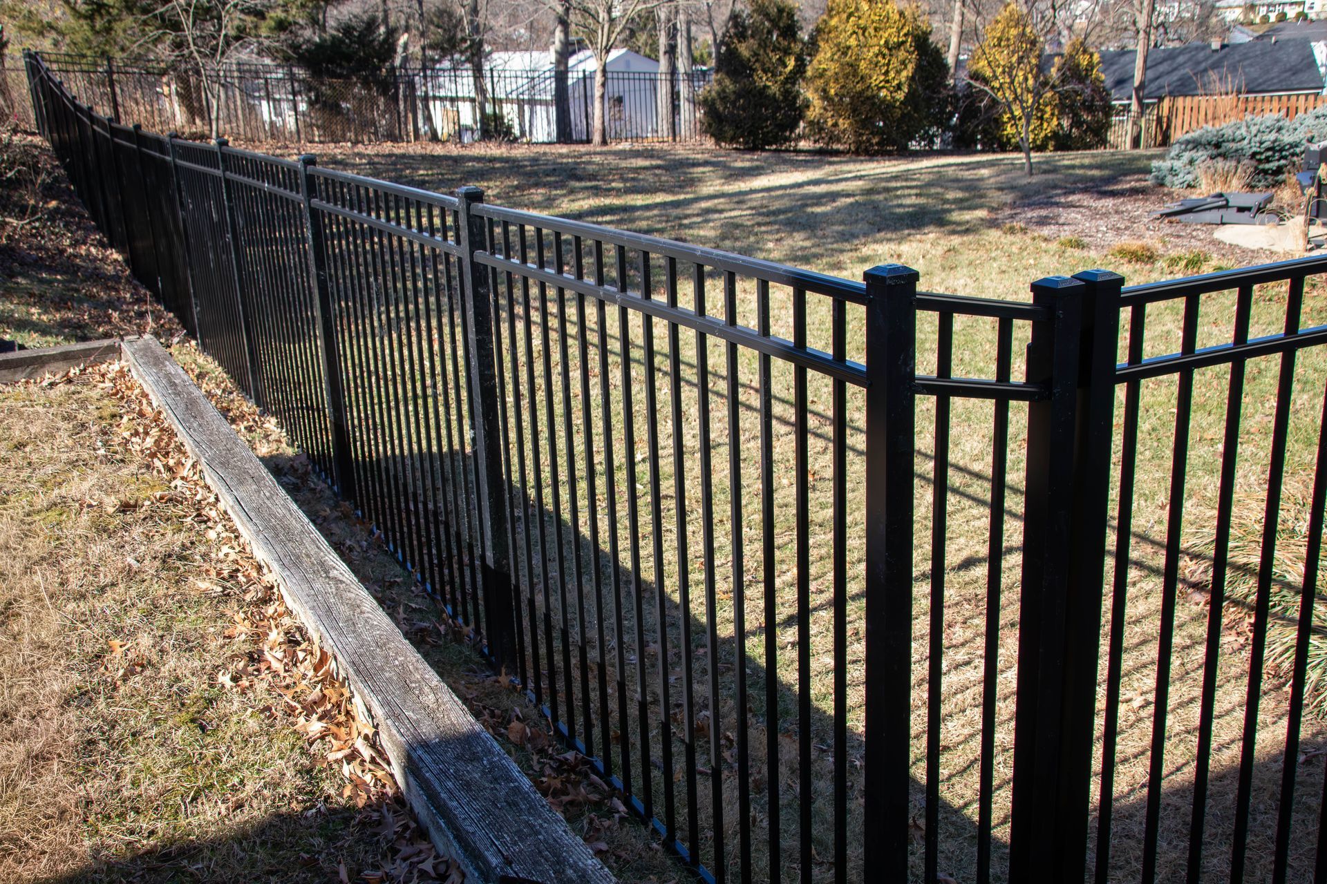 Black metal fence in a yard with grass and trees in the background.