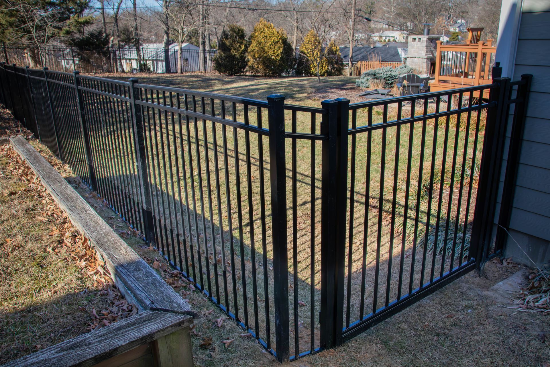 Black metal fence encloses a backyard; brown grass and wood trim.