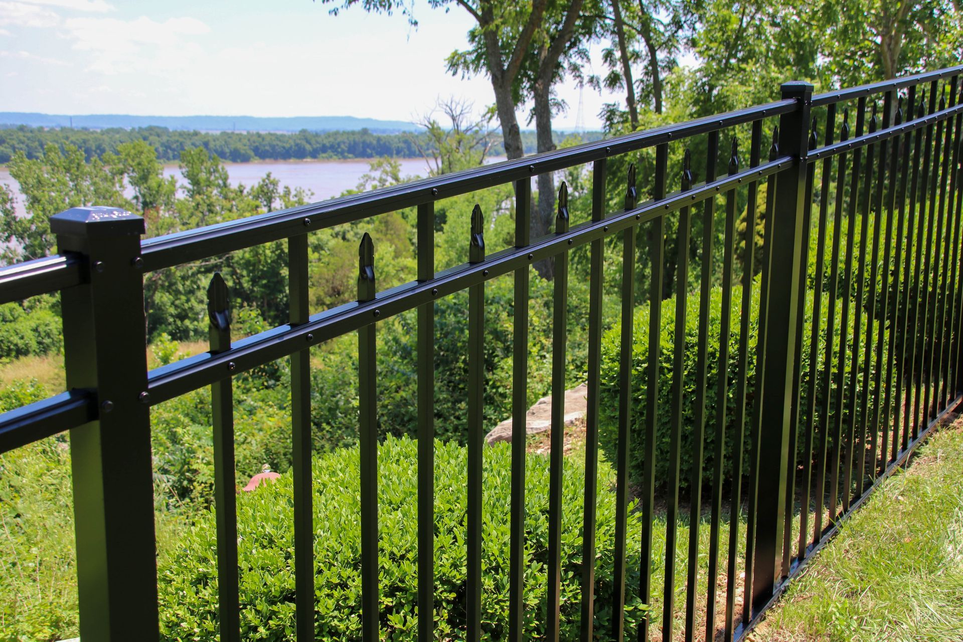 Black metal fence overlooking a river and trees on a sunny day.