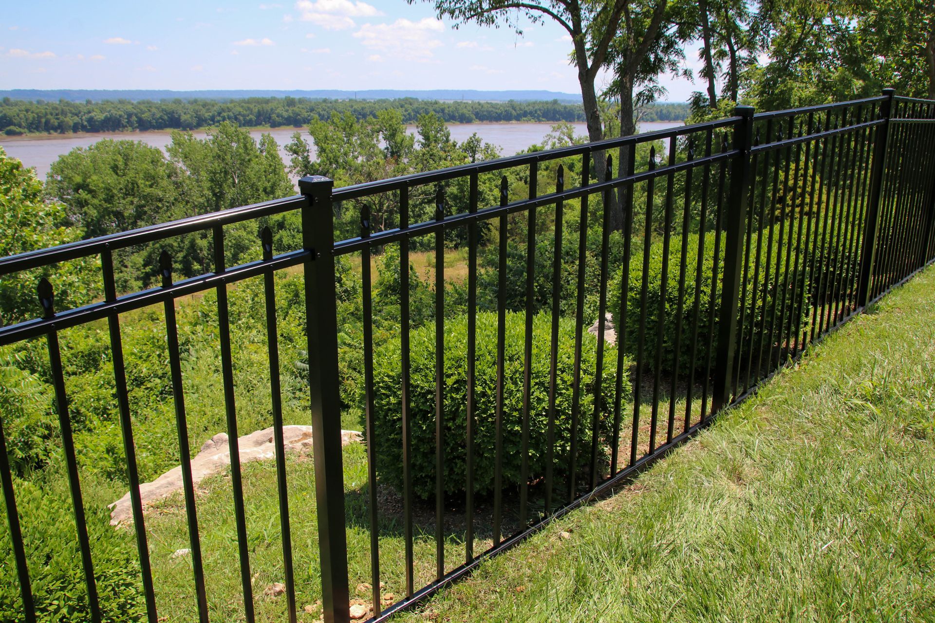 Black metal fence overlooking a river and trees on a sunny day.