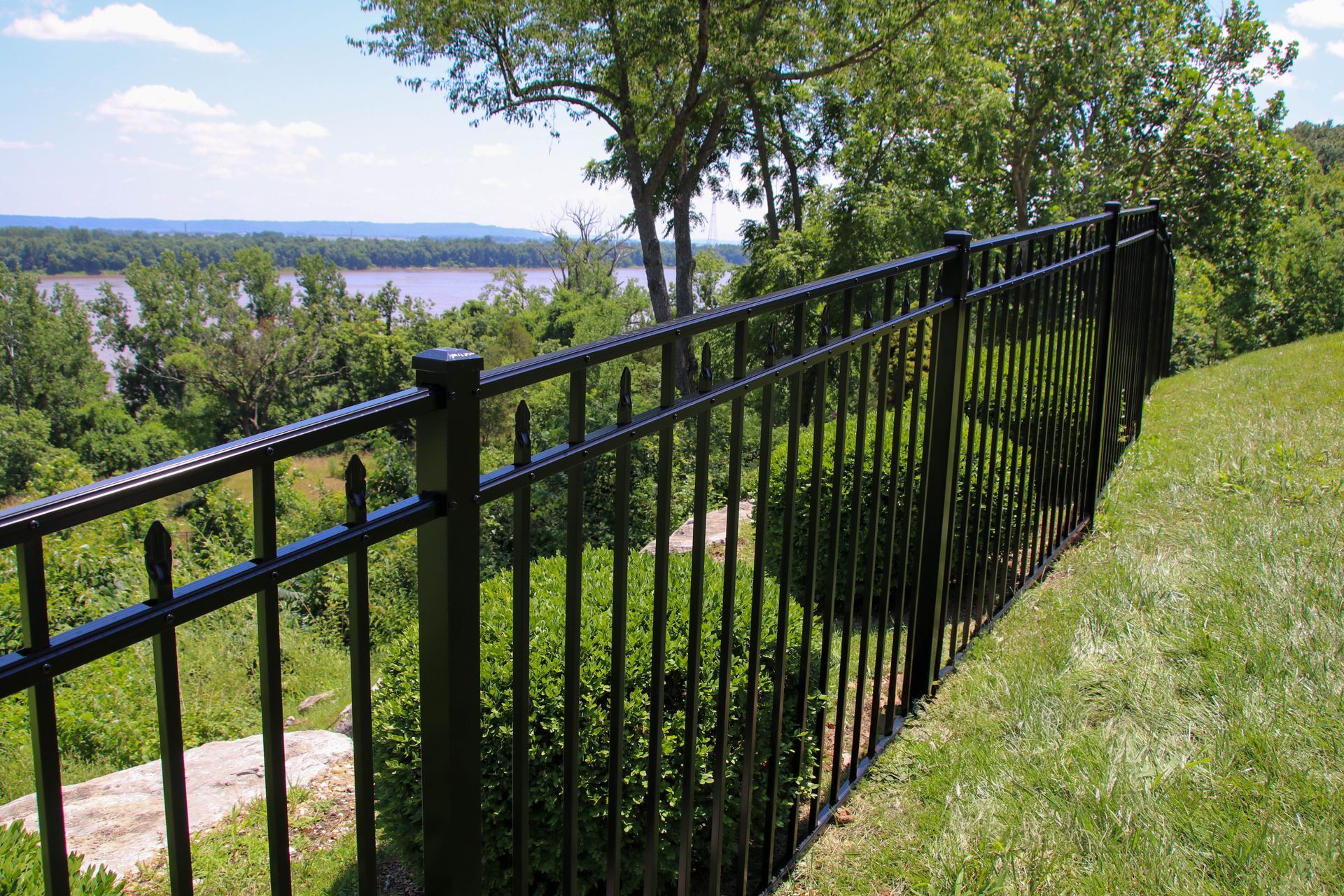 Black metal fence overlooking a river and trees on a sunny day.