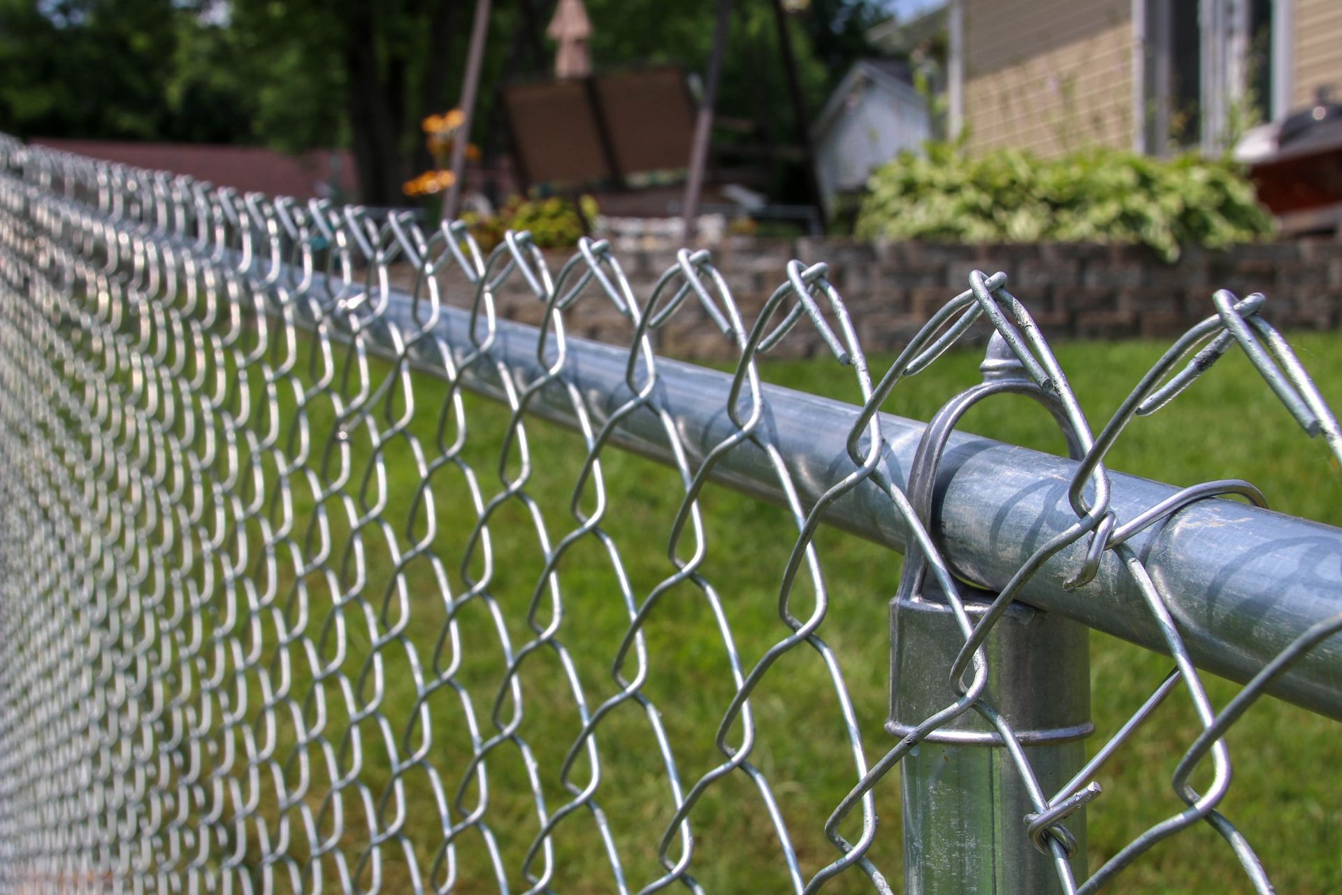 Close-up of a silver chain-link fence in front of a green lawn and a house.