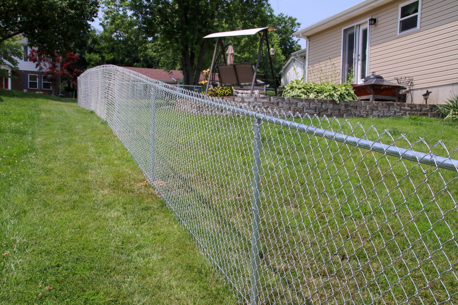 Chain-link fence in a backyard, beside a grassy lawn and a house. Swing set visible.