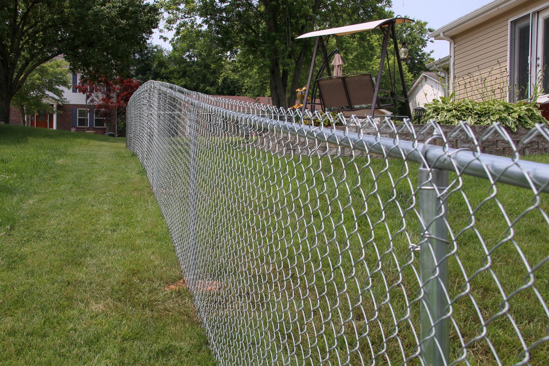 Chain-link fence in a grassy yard, with houses and a swing set in the background.