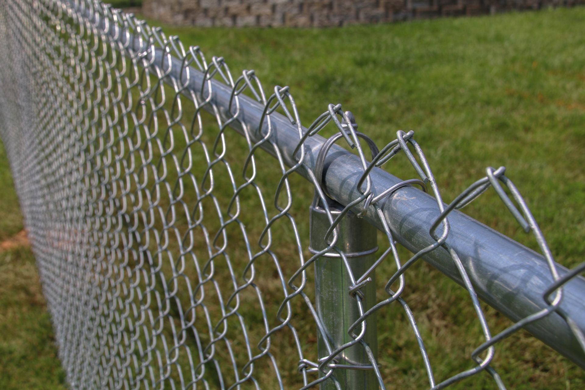 Chain-link fence with a silver top rail in front of green grass.